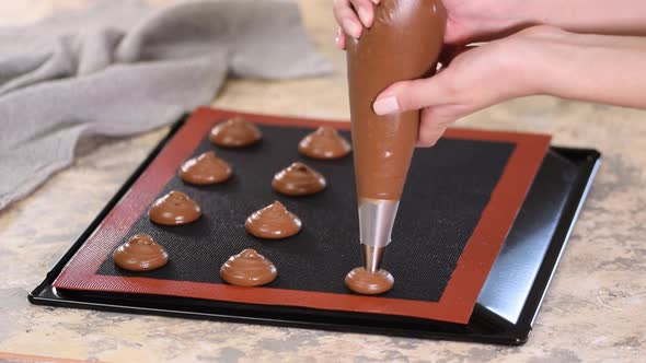 Cooking chocolate profiteroles, female hands squeeze the dough from the bag onto baking sheet