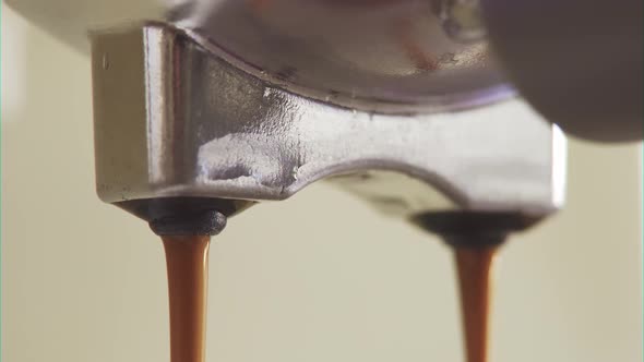 Drops of dark coffee drip through metal filter. Espresso flows out of machine. Brewing coffee