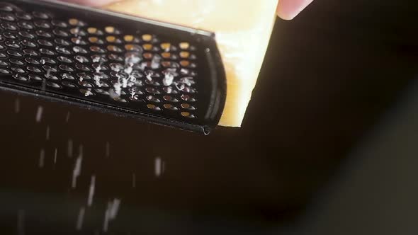 professional chef rubs Parmesan cheese on a metal grater.