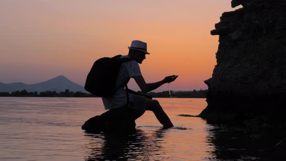 Silhouette of a Man Sitting on the Stone with Seascape on Background