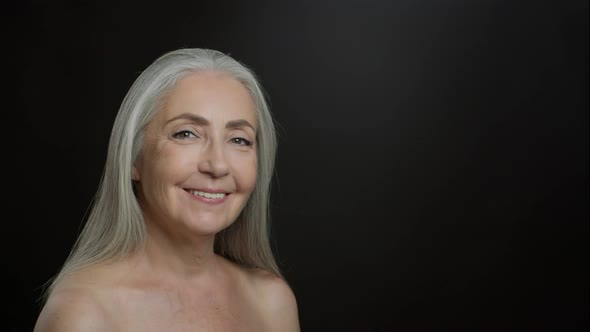 Beautiful Senior Lady Turning Face to Camera and Smiling Posing with Bare Shoulders Black Background