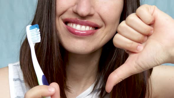 smiling young woman holding toothbrush and thumb down finger. bad choice toothbrush concept, better 