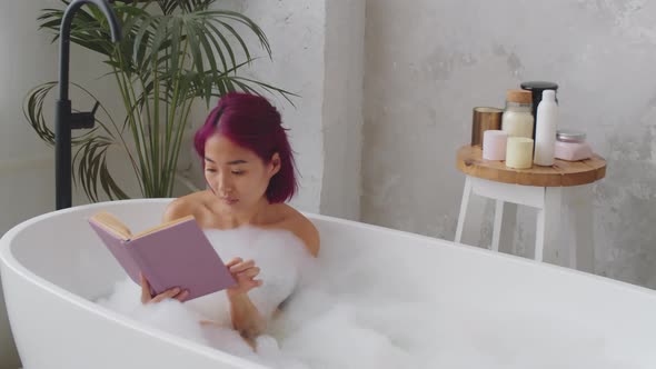 Asian Woman Sitting in Bathtub and Reading Book