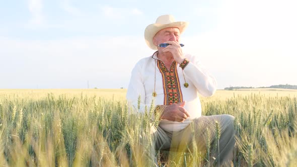 An Old Man in an Embroidered Coat and Hat Plays the Harmonica