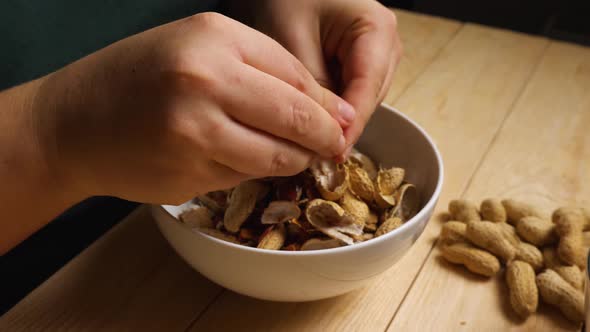 Close-up of a woman's fingers peeling peanuts from their shells over bowls