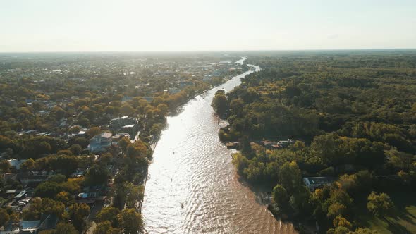 Aerial view of Lujan river with houses and trees at sides near sunset time. Jib down
