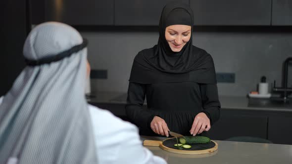 Portrait of Positive Middle Eastern Woman in Shayla and Abaya Cooking Salad in Kitchen Talking with