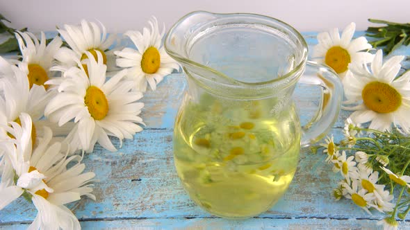 Brewing a herbal tea from chamomile in a glass jar on vintage light blue wooden tabletop.