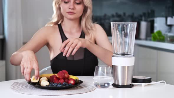 A young blonde woman making a milkshake of fruits and berries