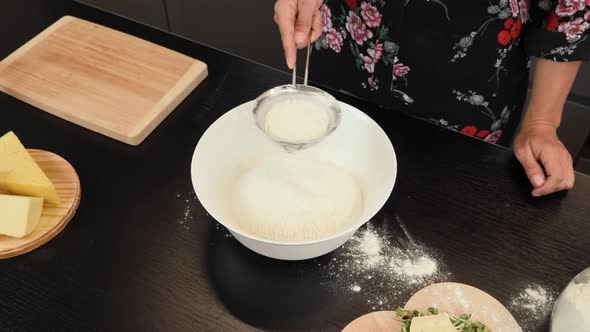 Sift flour through sieve while preparing dough for pizza.