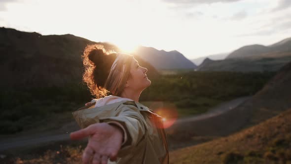 Free Happy Young Tourist in Green Raincoat Looking Up with Raised Arms Enjoying the Setting Sun in