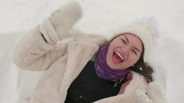 Young Woman Lies in the Snow and Laughs Cheerfully