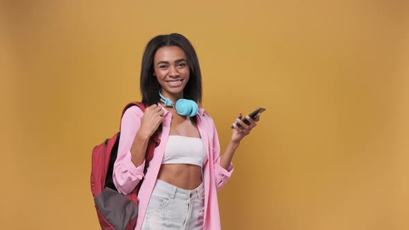 African American Student Woman Using Smartphone Standing Over Isolated Yellow Background with a