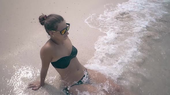 Water Covers Young Woman with Hair Bundle Lying on Beach