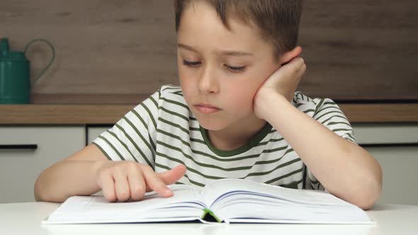 Portrait of a boy enthusiastically reading a book sitting at a table at home schooling.