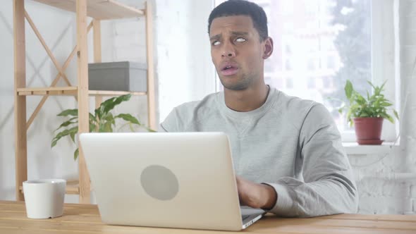 AfroAmerican Man Sitting in Office Upset By Loss Working on Laptop