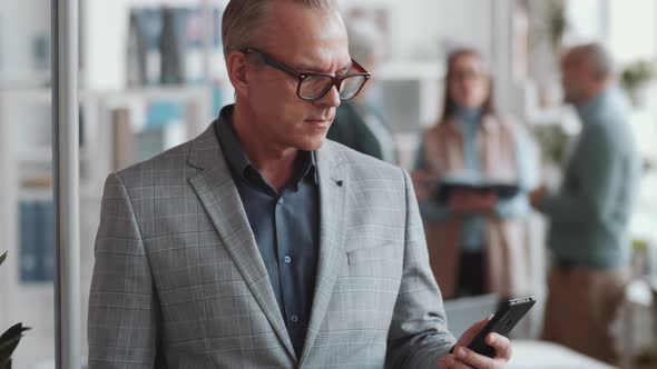 Joyous Businessman Using Smartphone and Posing for Camera in Office