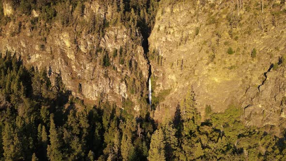 Aerial rising over Corbata Blanca thaw waterfall hiding between mountains surrounded by pine trees a