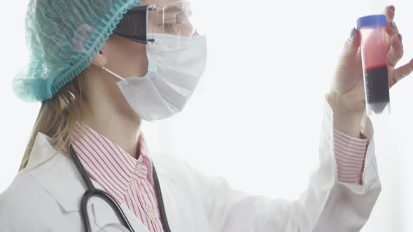 A Female Doctor in Medical Uniform is Holding and Viewing Test Tube with Blood Plasma Ready for