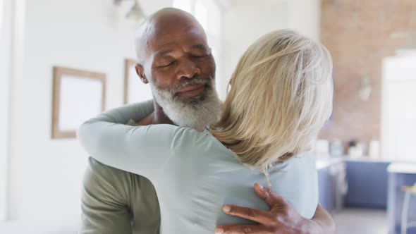 Mixed race senior couple hugging each other at home