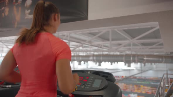A Young Girl in a Pink Tshirt Works Out in the Gym and Runs on a Treadmill