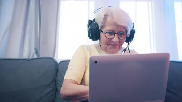 Elderly Woman with Headset Playing Video Games on the Laptop
