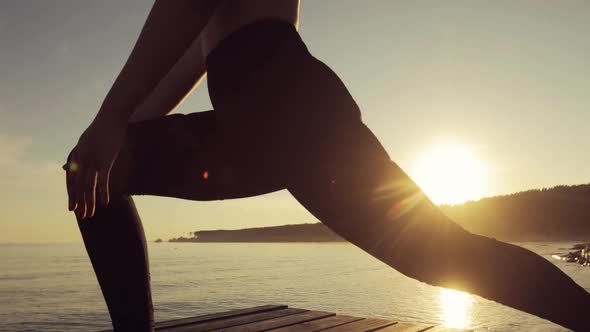 Woman Is Making Warrior I Pose Practicing Yoga on River Pier at Sunset, Side View.