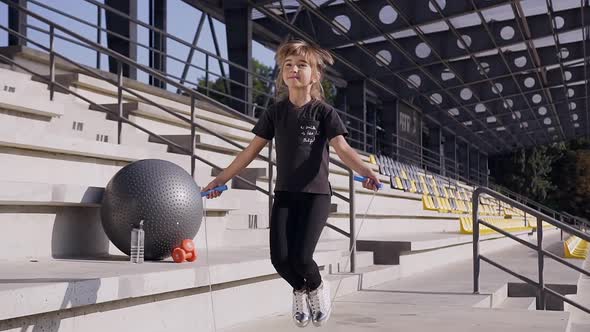 Little Girl with Ponytail in Black t-shirt and Leggings Jumping with Skipping Rope