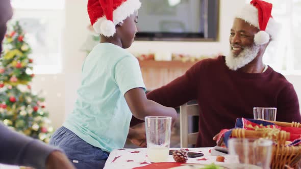 African american boy in santa hat hugging his grandfather while sitting on dining table having lunch