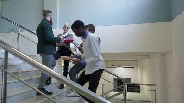 Side View African American Young Man Walking Upstairs Passing Caucasian Coworkers Discussing