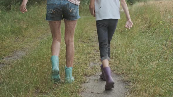 Two Happy Girls Sisters Walking After the Rain in Dirty Clothes Holding Hands Back View