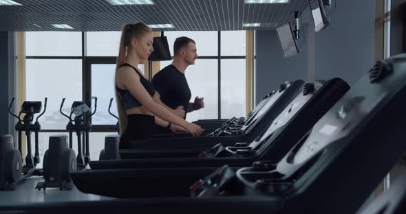 A Man And A Girl Go In For Sports In The Gym. Running On A Treadmill 
