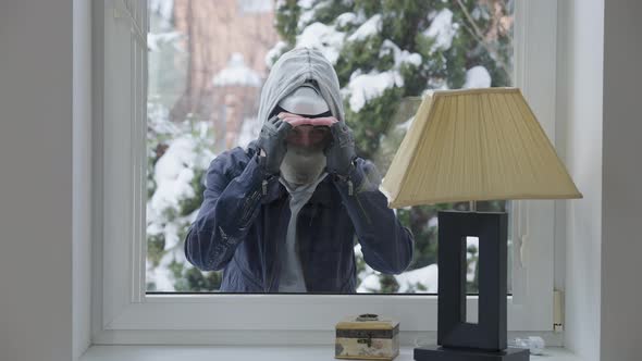 Portrait of Young Caucasian Male Burglar Looking Through Window Inside House