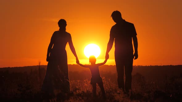 Child Plays with Dad and Mom on Field in Sunset Light