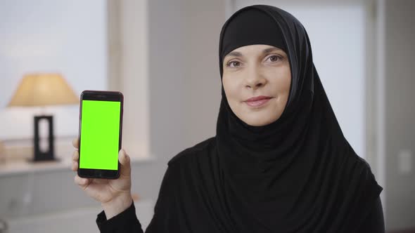 Close-up of Confident Muslim Woman in Black Hijab Holding Smartphone with Greenscreen