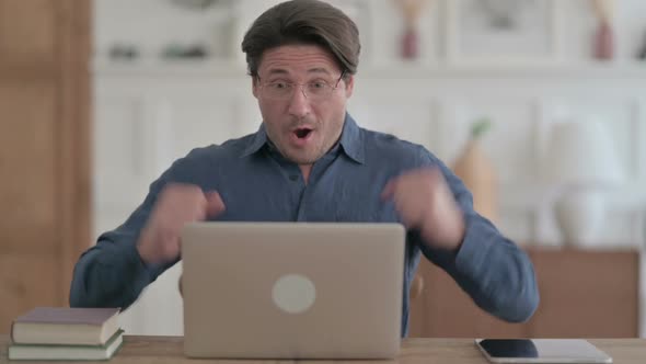 Young Man Celebrating Success while using Laptop in Office