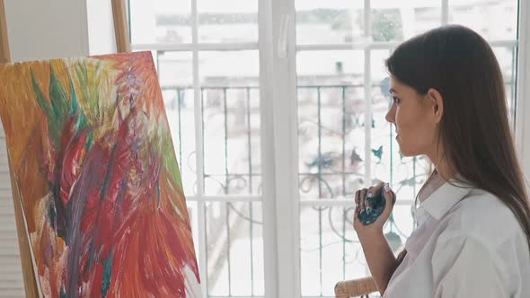Woman Artist with Palm in Paint Looks at Abstract Painting
