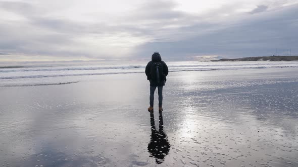 Man Standing On Wet Beach Watching Surf And Clouds