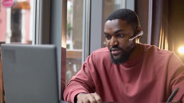 African American Young Man Wear Headset Communicating By Conference Call Speak Looking at Computer