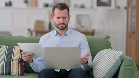 Angry Young Man Working on Documents and Laptop at Home, Frustrated