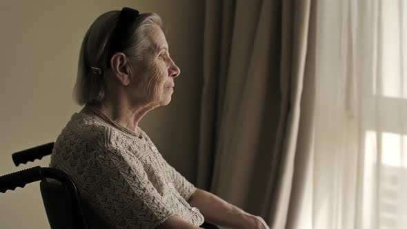 Disabled Elderly Woman Sit on Wheelchair and Looks Through the Window