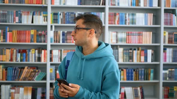 A Young Millennial Student with Glasses Flips Through the Social Network Feed on His Smartphone