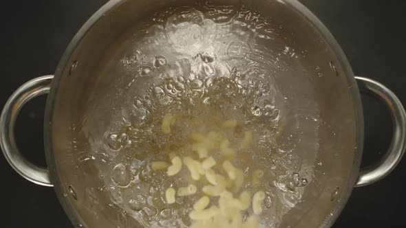 SLOW MOTION: Macaroni Pouring Into A Steel Pan With Boiling Water - Top View 
