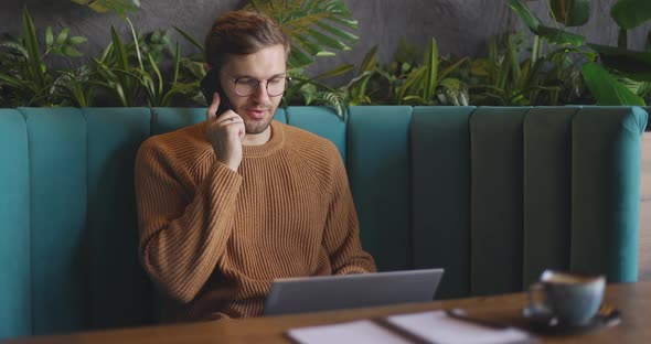 Man in Brown Sweater and Eyeglasses Sitting on Sofa and Talking on Mobile Phone and Working on