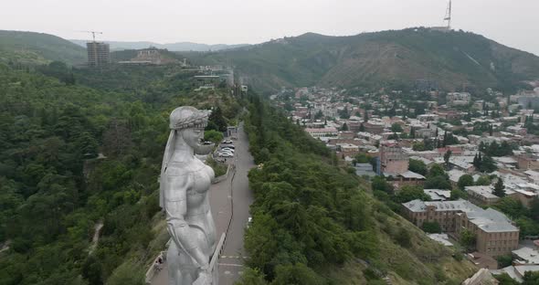 Arc aerial shot of the Kartlis Deda statue and Tbilisi during an overcast day.