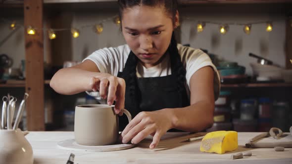 Young Woman Potter Trying on a Clay Handle to a Cup in Art Studio