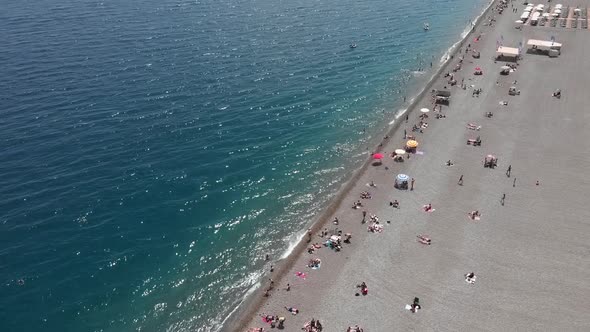 Wide pebble beach with people swimming and sunbathing.