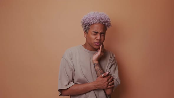 Dark Skinned Woman Suffers From Toothache Touches Cheek on Beige Background