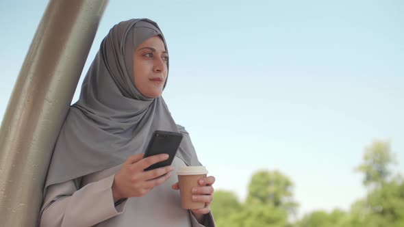 Muslim Woman with Smartphone and Coffee Outdoors