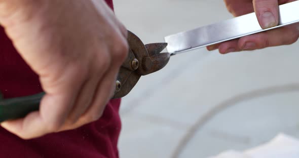 Close up of the hands of a construction worker using tin snips while cutting a piece of aluminum ang